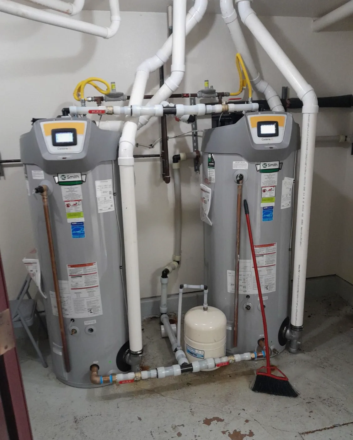 Two installed gas water heaters with connected pipework and an expansion tank